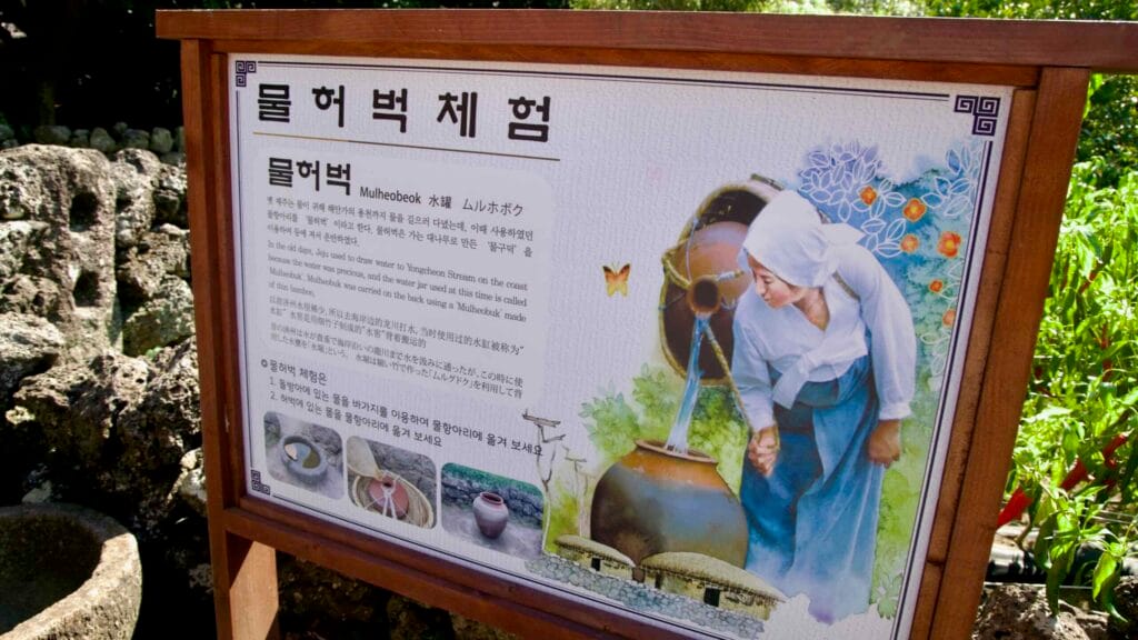 An exhibit sign explains the mulheobeok water jar at Jeju Folk Village with illustrations and multilingual text.