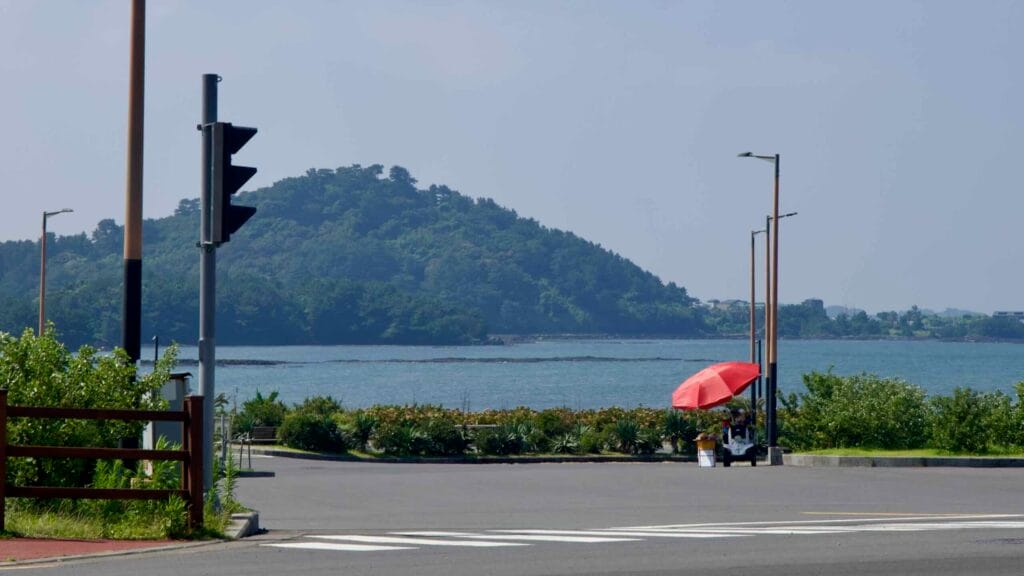 A quiet coastal intersection opens toward the sea, with a small islet and lighthouse.