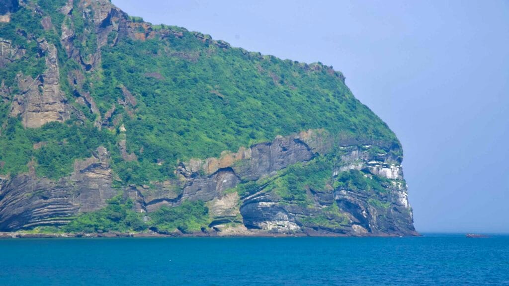 A close view of Seongsan Ilchulbong’s cliff shows stacked tuff and basalt layers cloaked in vegetation.