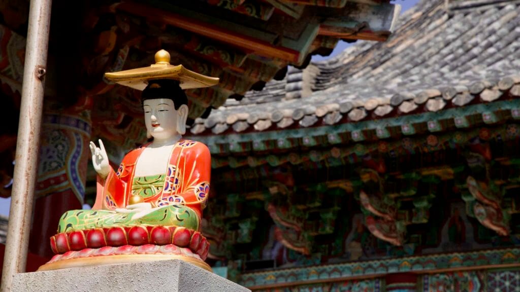 A colorful seated Buddha rests beneath carved eaves at Dongamsa Temple.