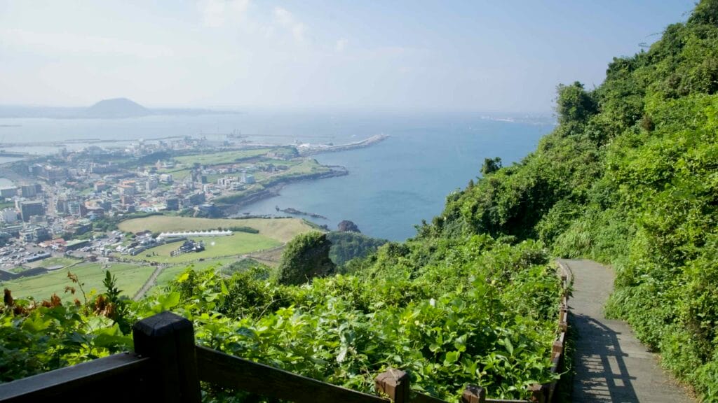 A hillside path overlooks Seongsan Port and the bright blue waters of the bay.