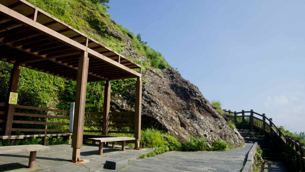 A wooden rest shelter stands beside the paved walking trail on Seongsan Ilchulbong.