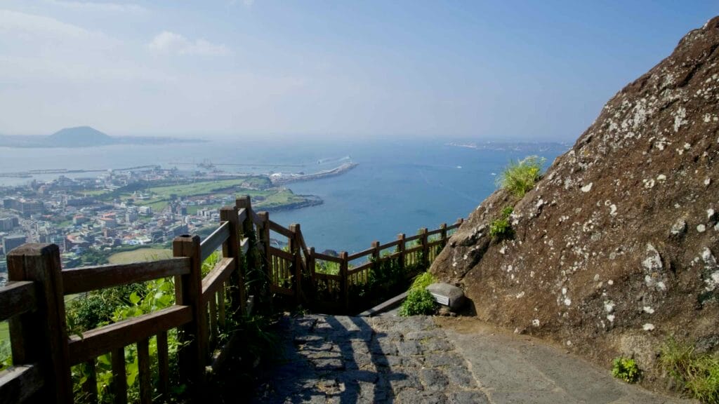 A railed stone path overlooks the harbor and breakwater from the Ilchulbong viewpoint.