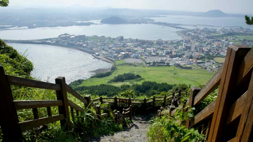 A steep wooden stairway zigzags down the hillside toward Seongsan-ri’s shoreline.