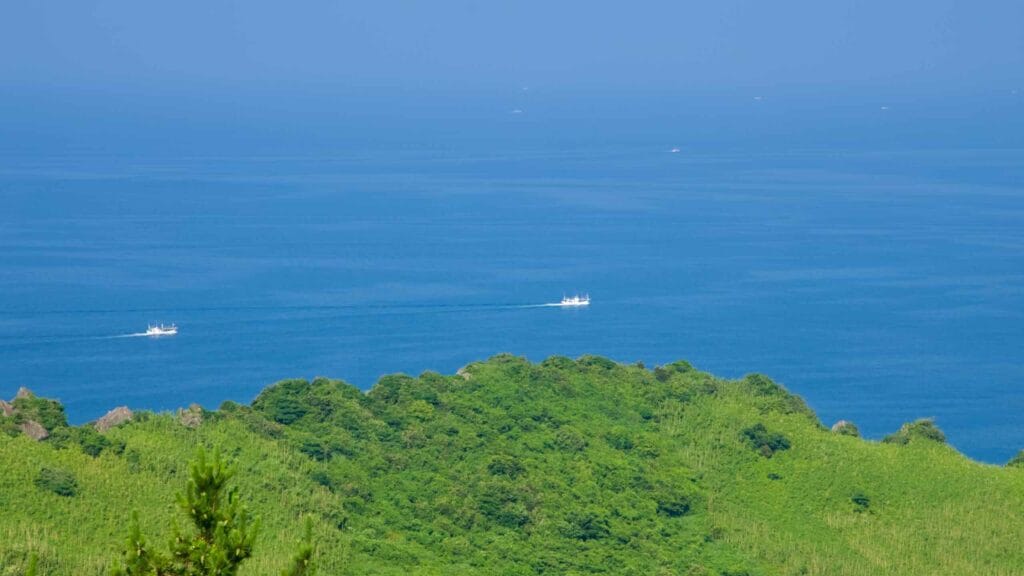 Small fishing boats leave faint wakes beyond Ilchulbong’s grassy crater rim.