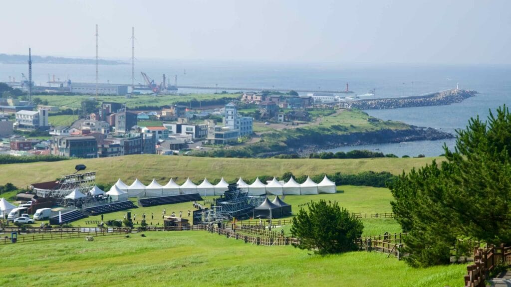 White festival tents and seating fill the amphitheater lawn below Seongsan Ilchulbong.