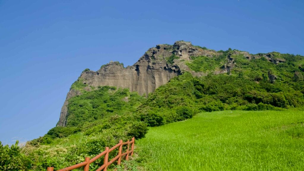 The tuff cliffs of Seongsan Ilchulbong rise in layered walls above grass and trees.
