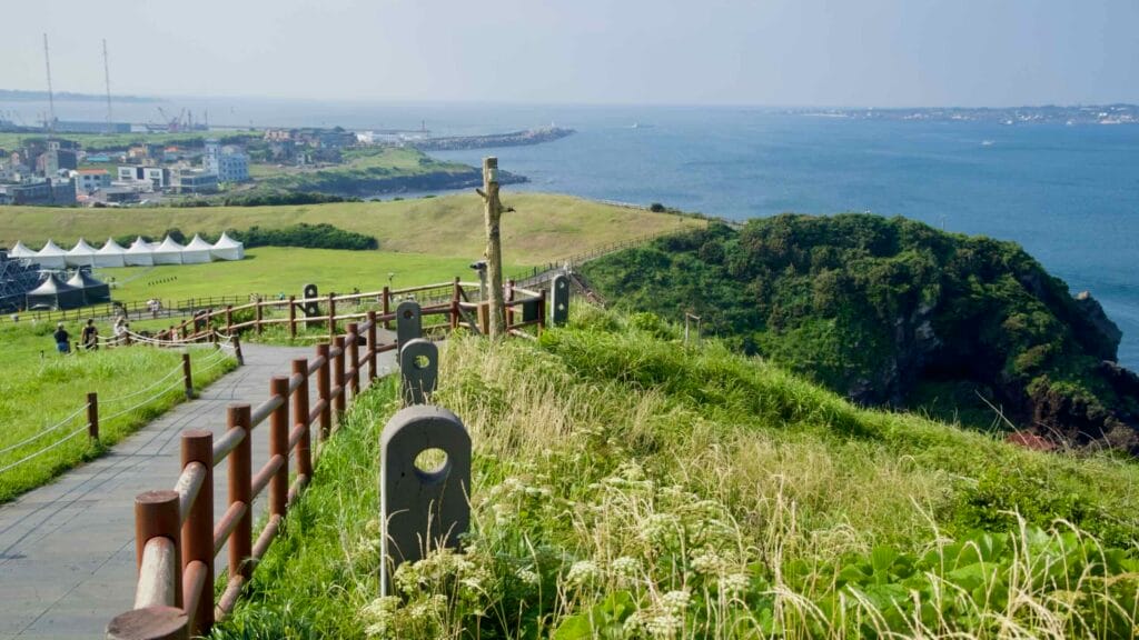 A coastal path bordered by rope and basalt posts curves along Seongsan Ilchulbong.