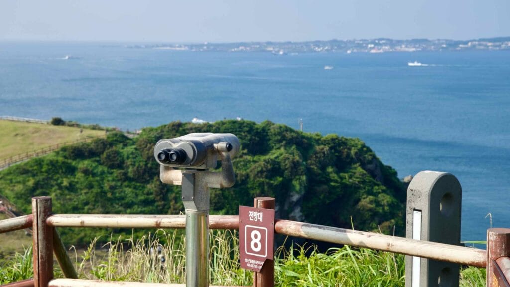 At Viewpoint 8 on Seongsan Ilchulbong, a coin binocular faces the headland and broad sea.