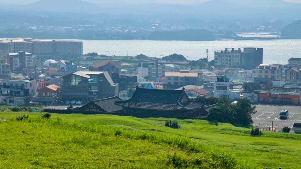 A traditional tiled roof nestles in green fields below Seongsan Ilchulbong.