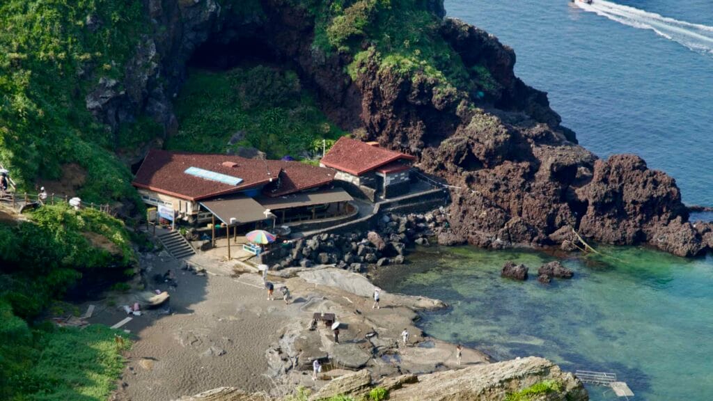 Umutgae Coast’s cove sits below Seongsan Ilchulbong, with lava platforms and a haenyeo house.