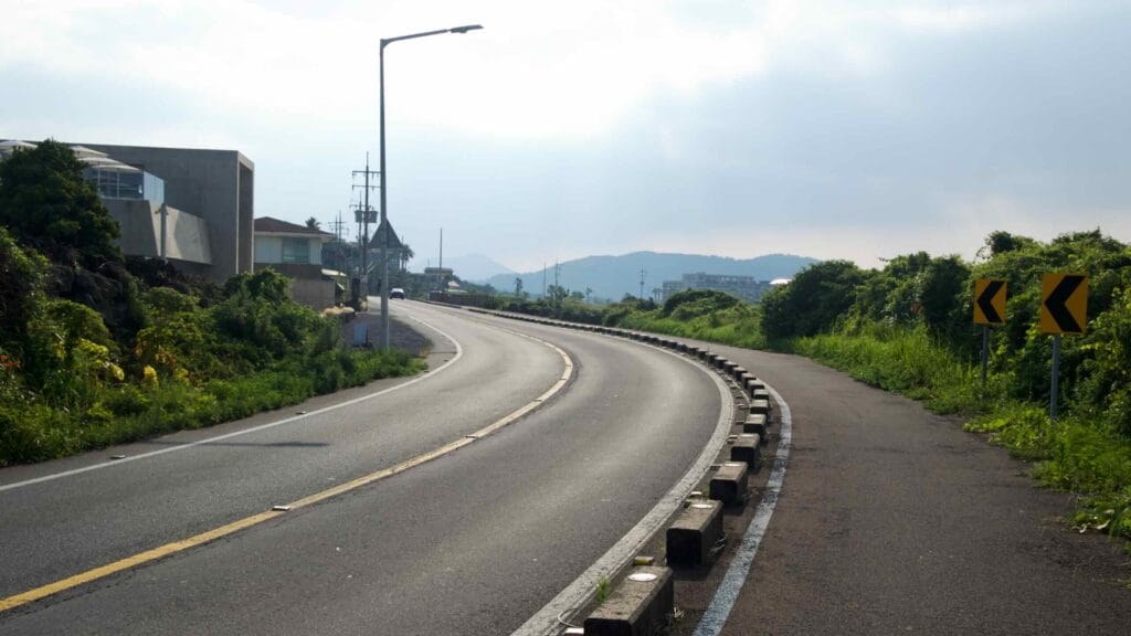 A sweeping coastal road curves past hedges and homes, with a parallel bike and walking path.