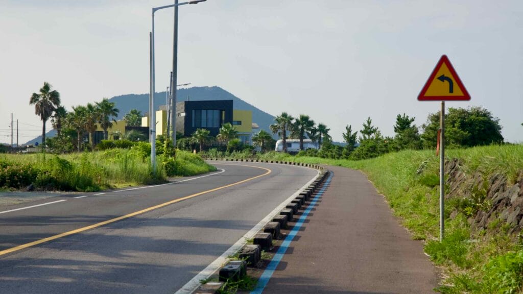 A coastal bend and bike lane lead toward a distant volcanic oreum under open skies.