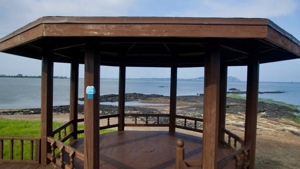 A wooden pavilion overlooks the basalt shore and tidal flats at Songnan Port on Jeju’s northeast coast.