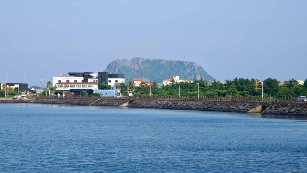 Ojo Village rests below Seongsan Ilchulbong with seawalls and a coastal road curving across Songnan Port.