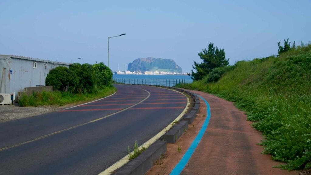 A road and bike path curve toward the sea with Seongsan Ilchulbong in view ahead.