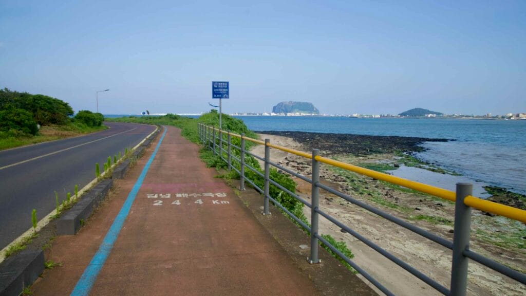 The Jeju cycle path runs above a basalt shore at Songnan Port facing Sunrise Peak.