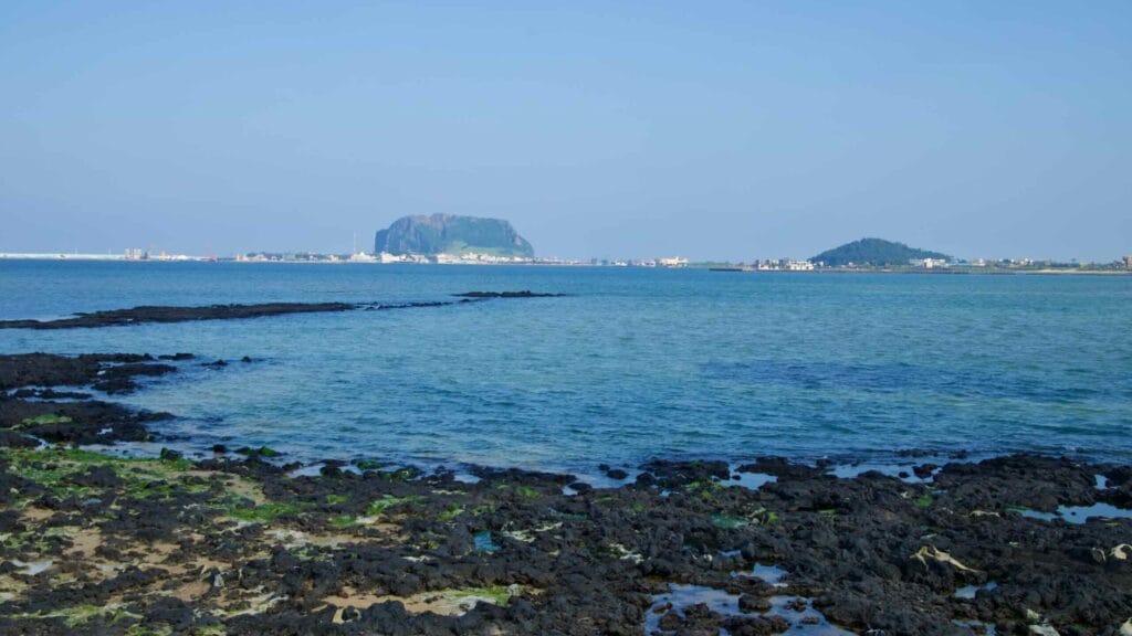 Basalt tongues stretch from Songnan Port toward the sea with Seongsan Ilchulbong beyond.
