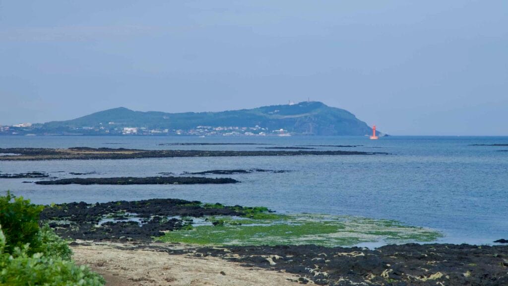 A coastal bike path runs above the rocky shore at Dumun Port with Udo Island visible beyond.