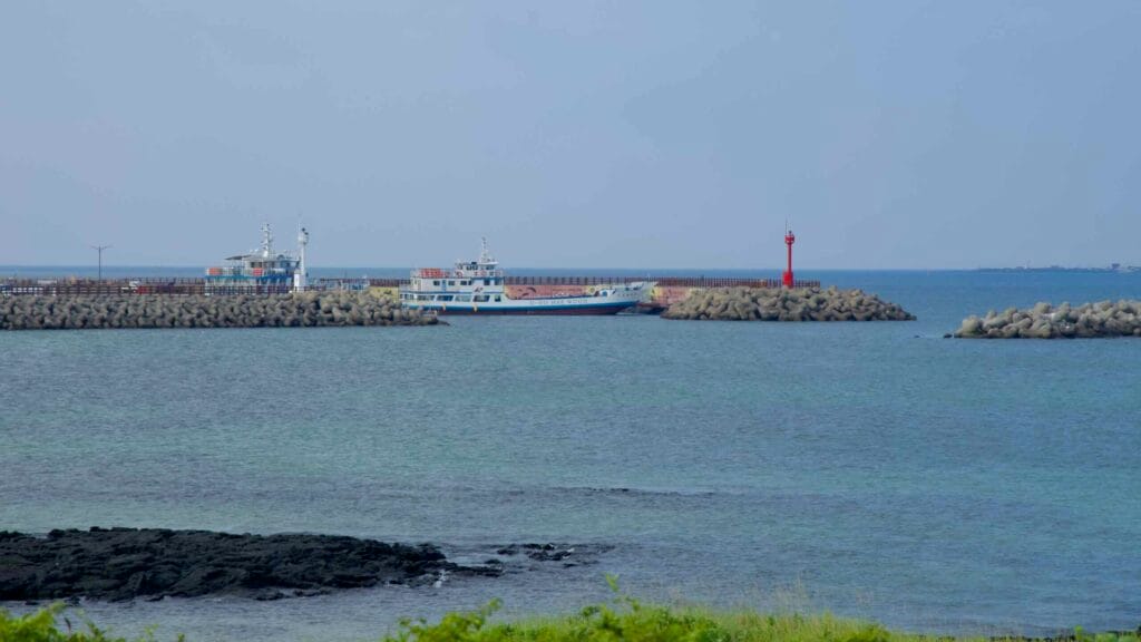 A Udo ferry waits behind the breakwater at Dumun Port beneath a bright red harbor light.