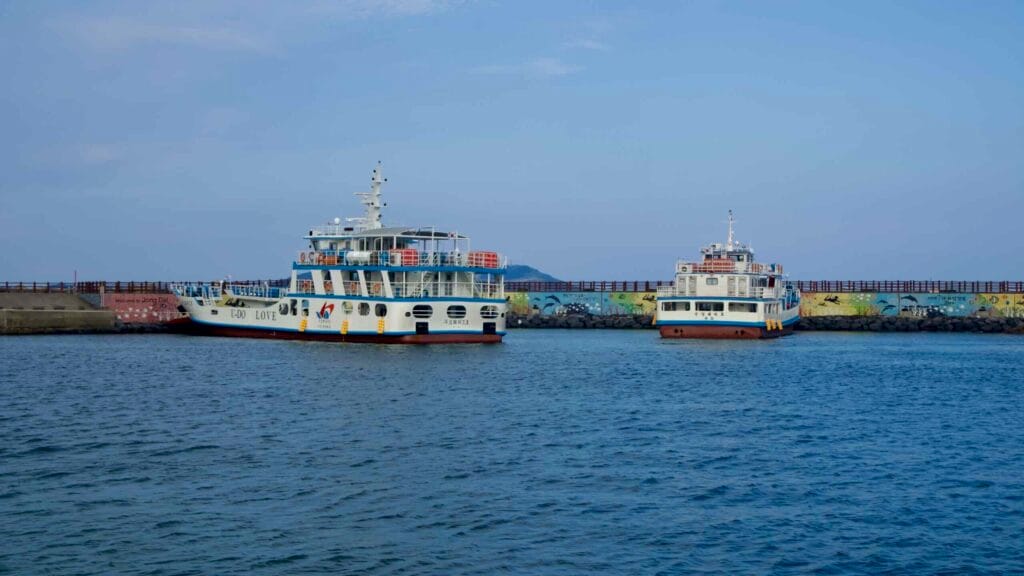 Twin Udo ferries idle inside Dumun Port beneath a seawall decorated with a mural.