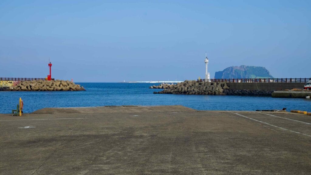 Red and white harbor lights frame the channel at Dumun Port, with Seongsan rising beyond.