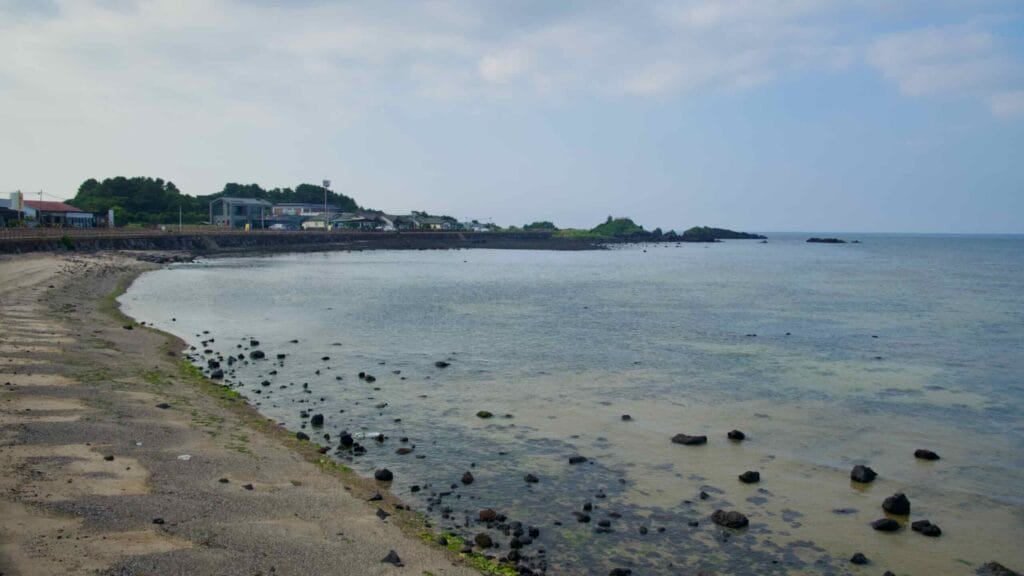 A curving bay near Dumun Port reveals clear shallows glimmering over dark volcanic rock.
