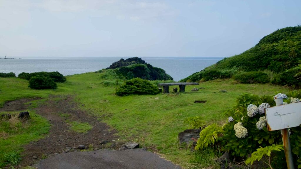 A grassy overlook with a stone bench faces the open sea at Gomangnandol Rest Area.