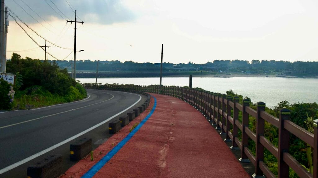 A wooden-railed red path follows the rocky shoreline toward Hado Beach.