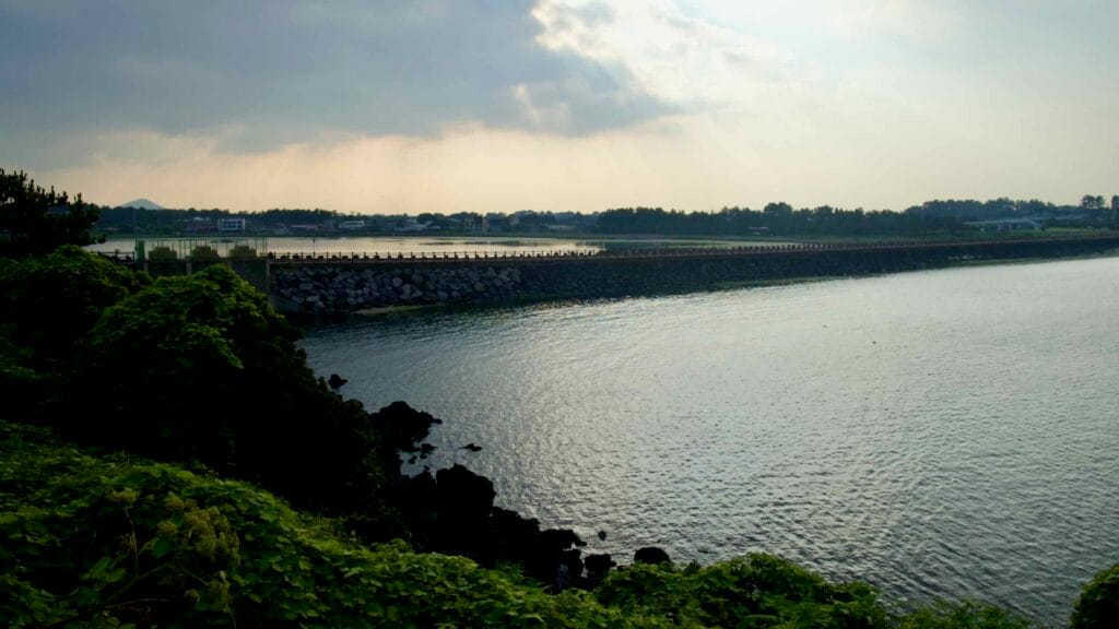 A sheltered inlet and long stone causeway protect the shallow, sunlit bay at Hado Beach.