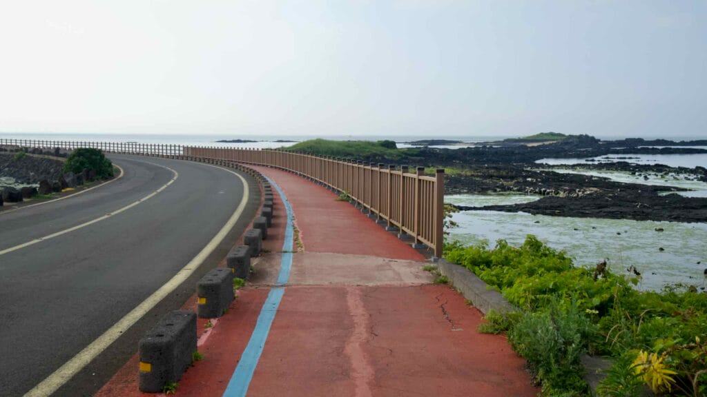 A red bike path follows the basalt shoreline toward Tokkiseom’s low green islets.