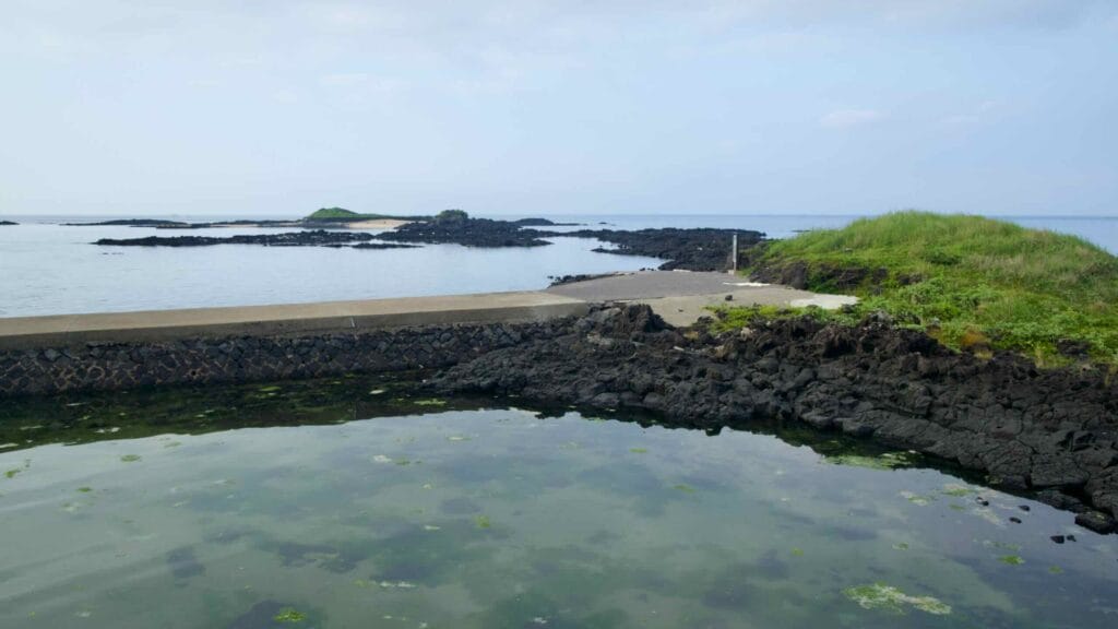 From the seawall, Tokkiseom’s grassy islet rises beyond black lava reefs and tide pools.