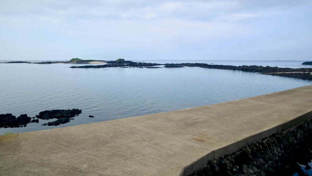 A concrete harbor wall points toward Tokkiseom and its pale sandy patch offshore.