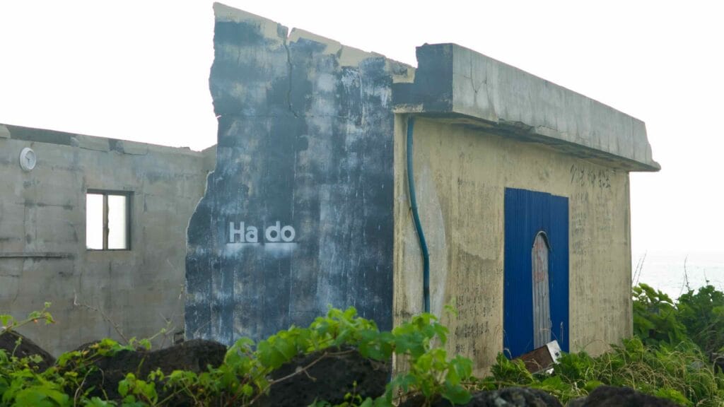 A weathered concrete building with faded “Hado” lettering stands by the sea.