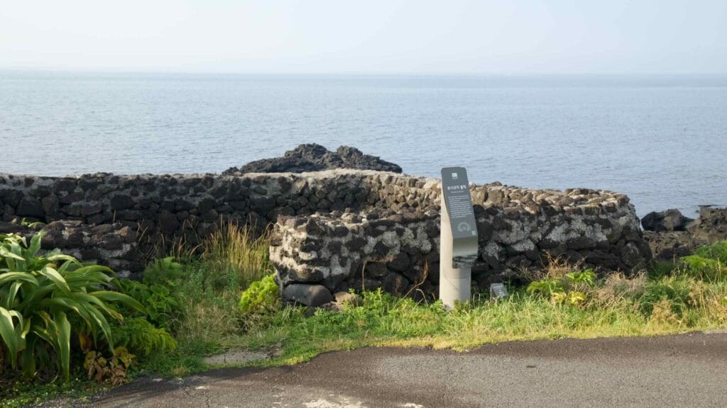 A low stone enclosure with an interpretive marker stands above the rocky coast.