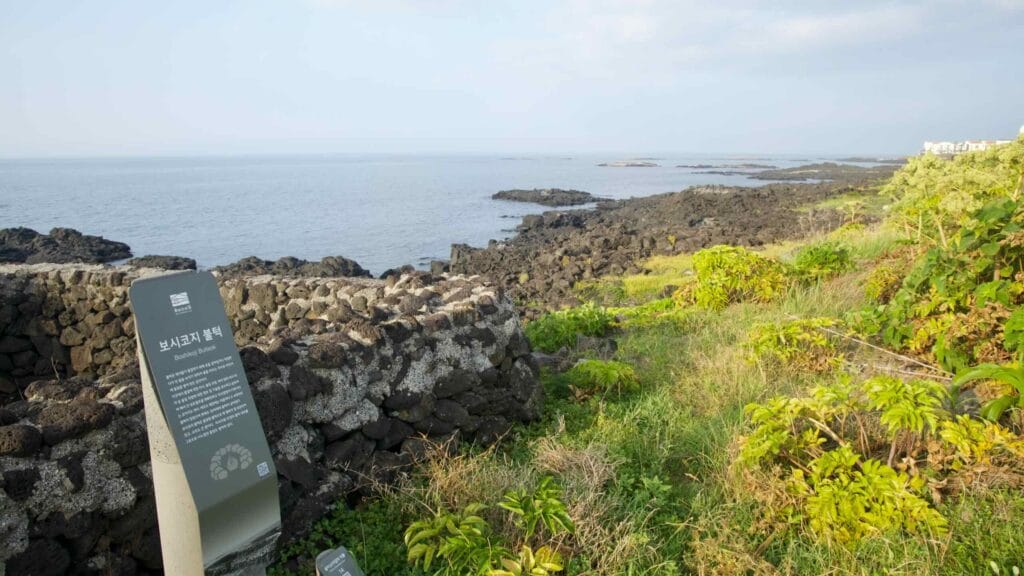 Basalt walls and an interpretive marker line the shore near Byeolbangjin Fortress on Jeju’s northeast coast.
