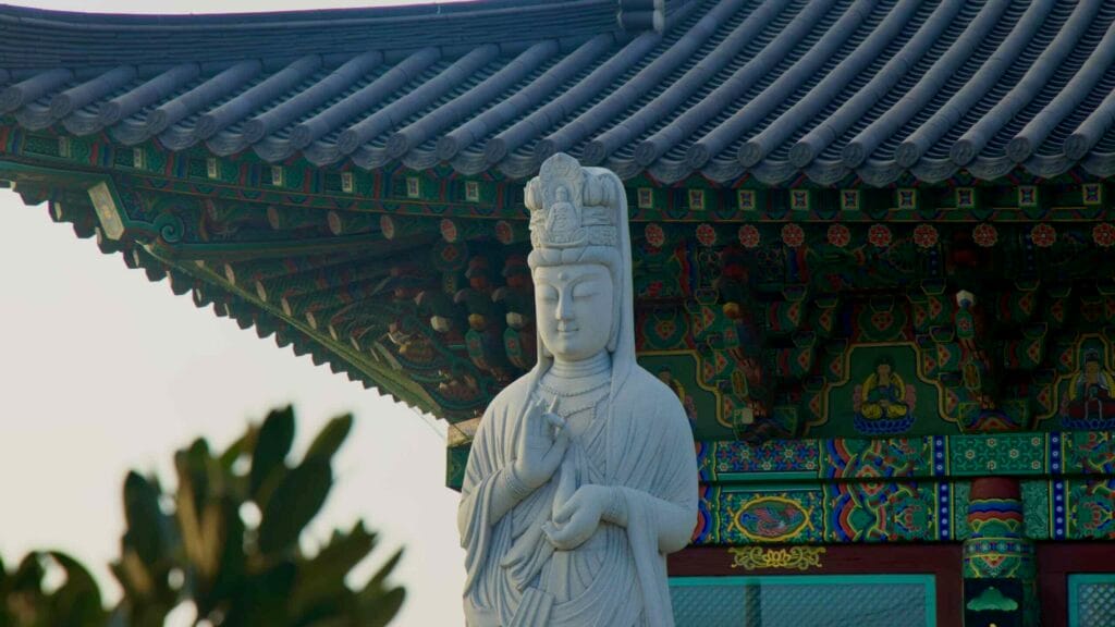 A white bodhisattva statue stands beside the colorful eaves of Yongmunsa Temple.