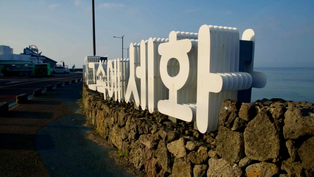 Large white “Sehwa” lettering sits on a basalt seawall beside the harbor walkway.