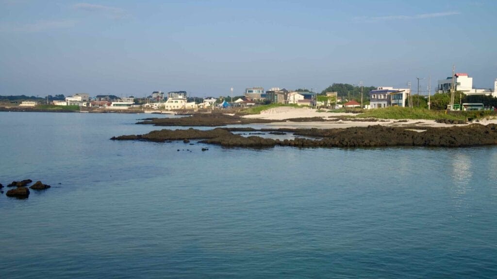 White sand and black lava ledges frame the bright blue bay at Sehwa Beach.