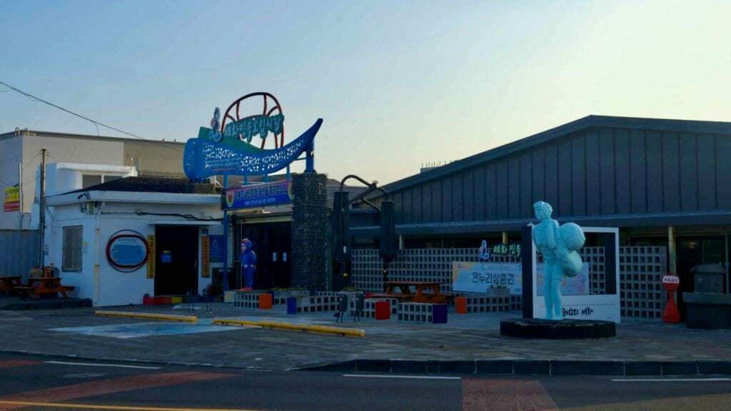 The entrance to Sehwa Folk Five-Day Market features a sign and a haenyeo statue.