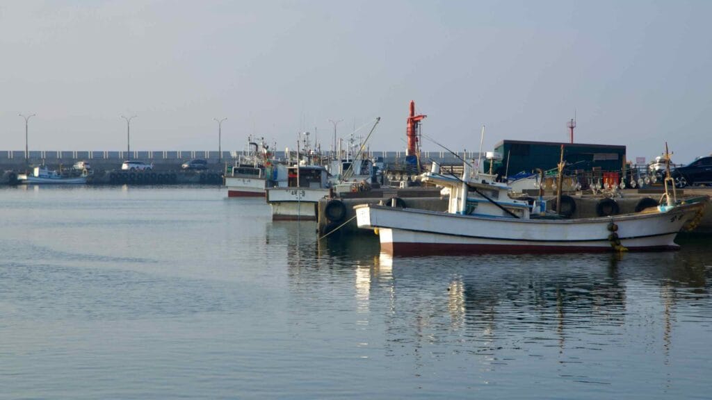 Red and white beacons stand above Sehwa’s breakwater with moored boats below.