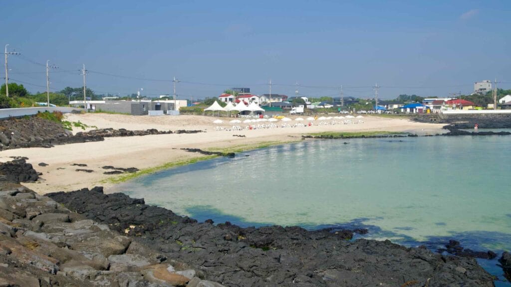 A quiet morning on Pyeongdae-ri Beach shows a shallow cove with white sand and black lava rock.