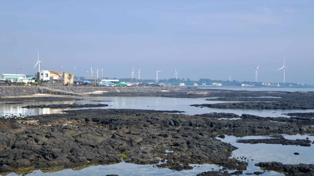 Tidal pools on the Handong-ri shore reflect a line of wind turbines.