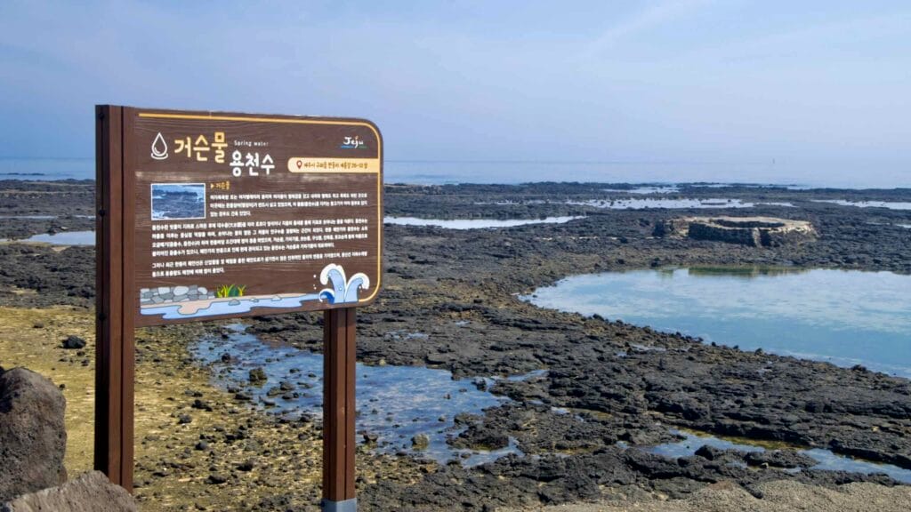 A sign for Geoseunmul spring faces tidal pools and the circular basin on the Handong lava shore.
