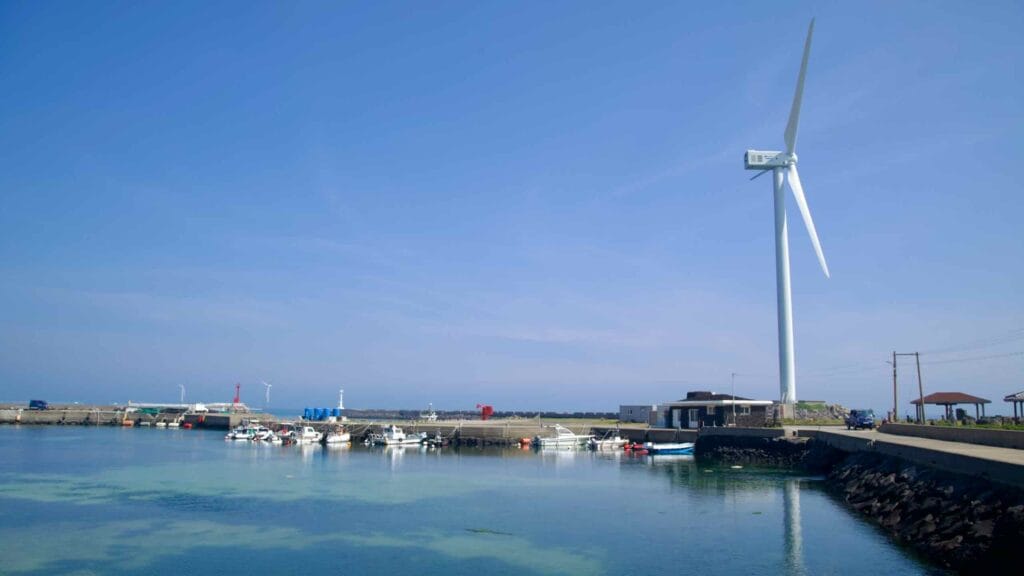 Fishing boats rest in the sheltered basin at Haengwon Port beside a tall wind turbine.