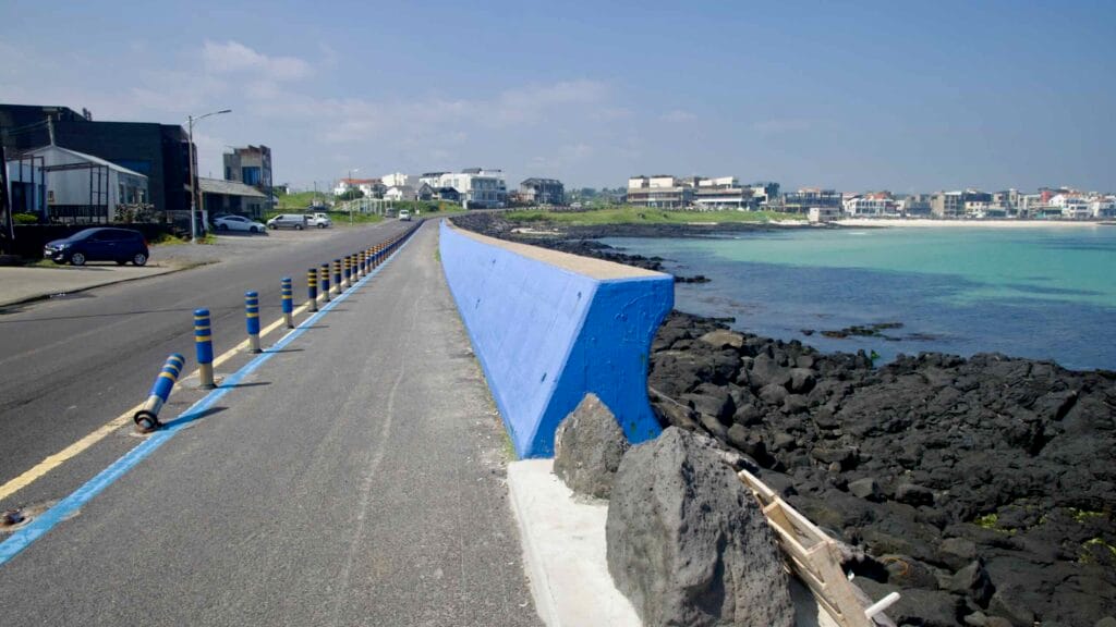 A blue seawall and cycling lane follow Woljeongri’s basalt shoreline.