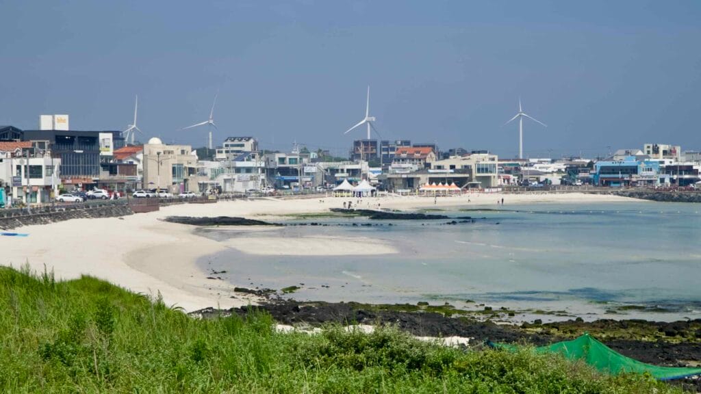 Wind turbines rise behind Woljeongri’s white‑sand beach and cafes.