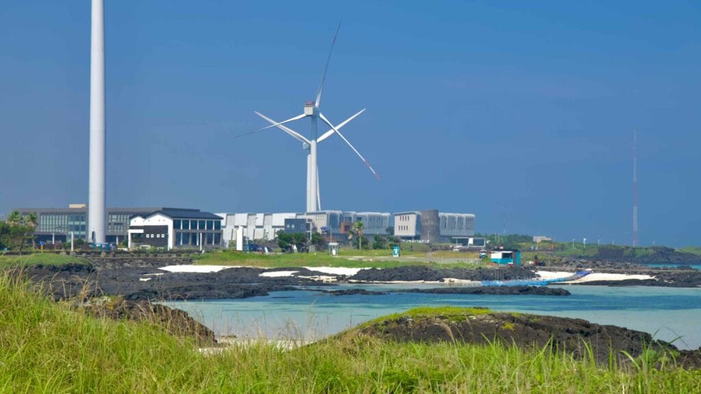 A coastal wind turbine rises beside modern buildings and lagoons.