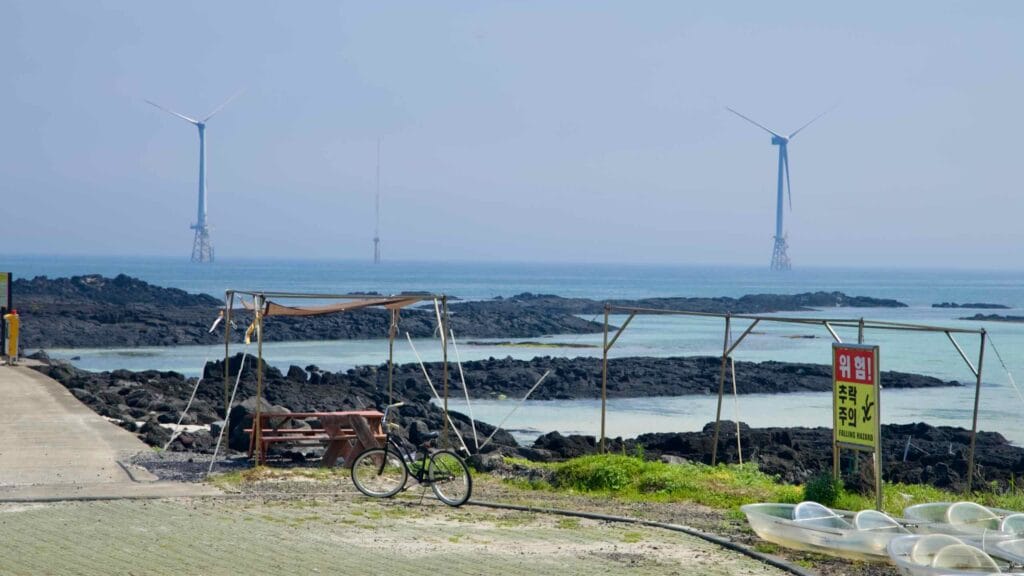 A shore shelter faces basalt reefs and offshore wind turbines.