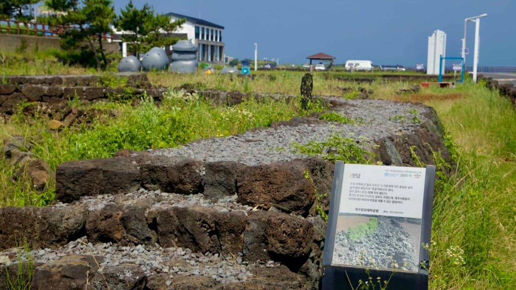 Stone‑wall terraces and an info board line a grassy path.